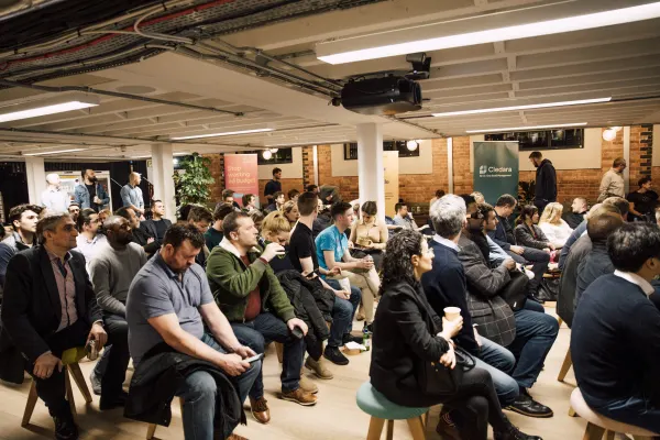 Live at SaaStock Local London — wide side view of the seated audience with the Cledara 'Your All-In-One SaaS Management' pull-up banner visible to the right, brick walls and industrial ceiling overhead