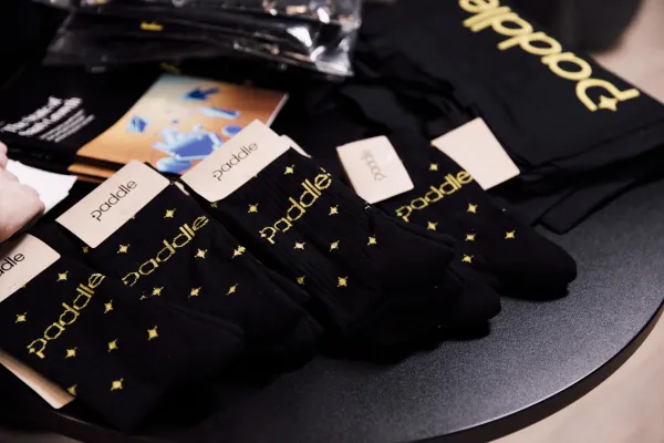 Live at SaaStock Local London — branded Paddle socks (black with gold 'paddle' wordmark) laid out on the sponsor swag table