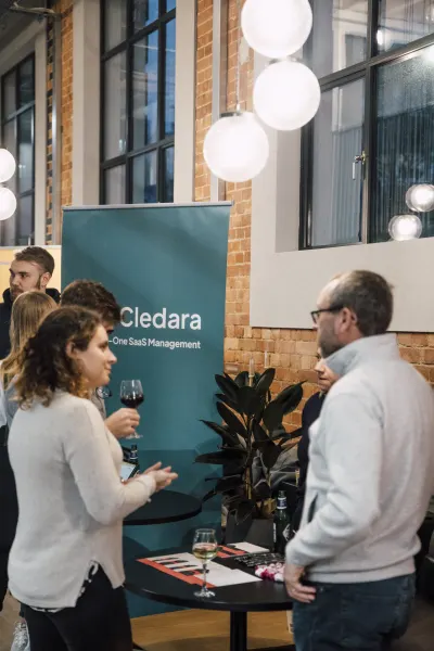Live at SaaStock Local London — Cledara 'Your All-In-One SaaS Management' pull-up banner with founders networking in front of it over wine and beer