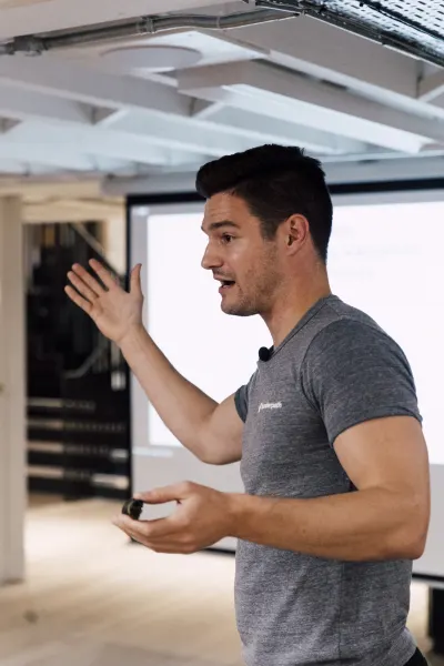 Live at SaaStock Local London — speaker in a gray t-shirt mid-gesture with one hand raised, presenting in front of the projection screen