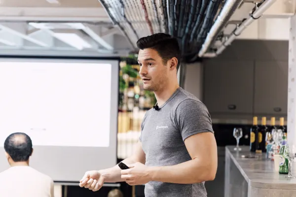 Live at SaaStock Local London — same speaker in a gray t-shirt mid-presentation, with the venue bar (wine bottles and water lined up) behind him